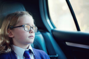 Child with glasses sitting in a car staring out the window