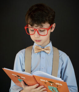 A young boy with glasses reading a book.